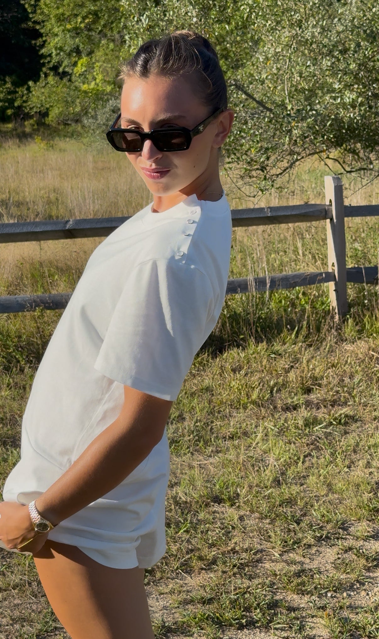 Woman wearing sunglasses and a white t-shirt onesie outfit.