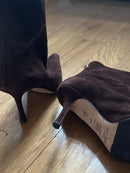 Brown high-heeled boot on a wooden floor.